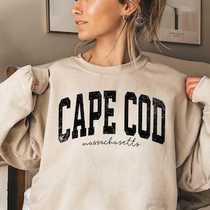 Op de afbeelding: Een beige sweatshirt met de tekst "CAPE COD Massachusetts" in zwarte letters.