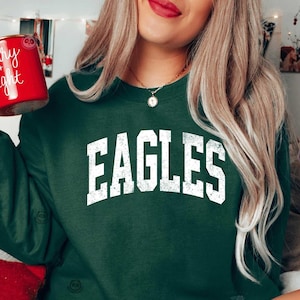 May include: A dark green sweatshirt with the word 'EAGLES' printed in white on the front. The sweatshirt has a distressed, vintage look.