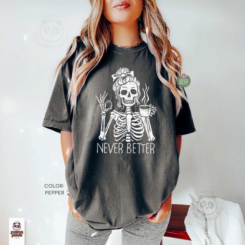 May include: A pepper-colored t-shirt featuring a white graphic of a skeleton with a messy bun hairstyle, holding a coffee cup and making an okay hand gesture. The text "NEVER BETTER" is printed in white below the skeleton illustration.