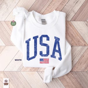 May include: White sweatshirt with the word "USA" in distressed blue lettering and a small American flag graphic. The word "WHITE" is printed below the sweatshirt.