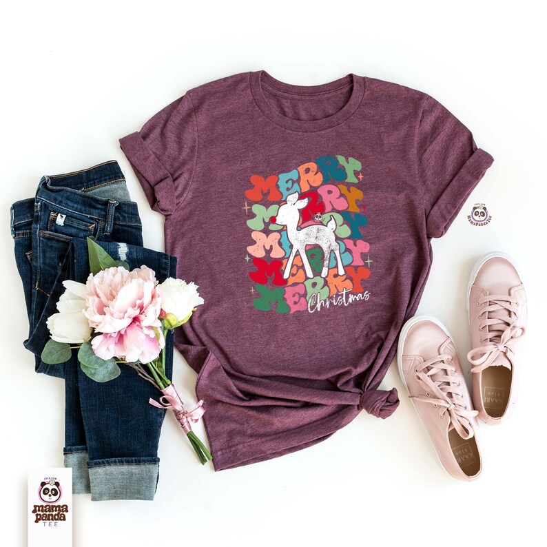 May include: A maroon t-shirt with a colorful graphic of the word "Merry" repeated multiple times with a white reindeer in the center. The text "Christmas" is below the graphic.