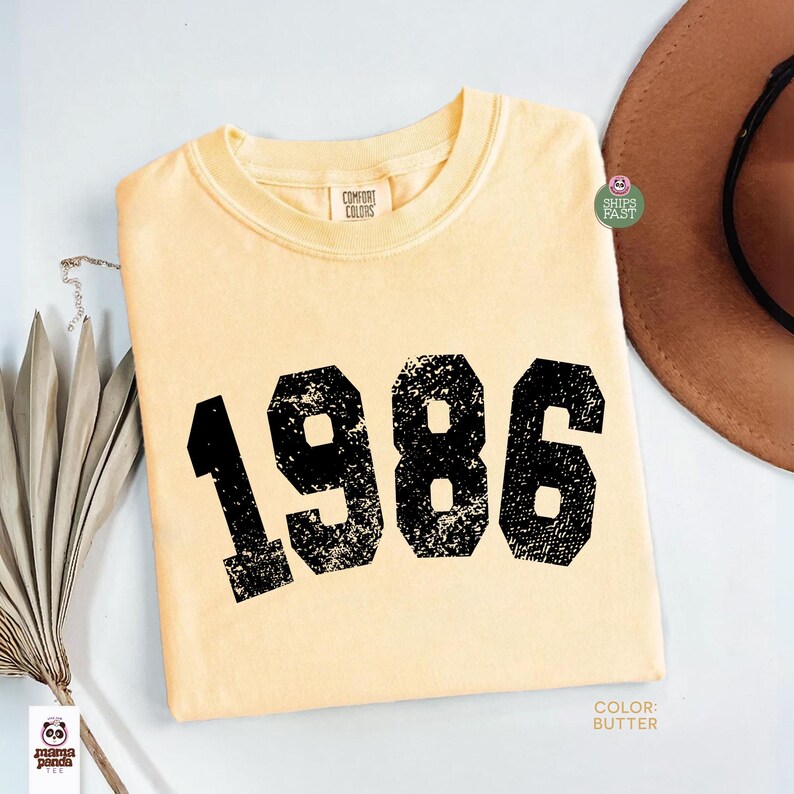 Może przedstawiać: Jasnoż&oacute;łta koszulka Comfort Colors z rokiem "1986" wydrukowanym dużymi, czarnymi, zniszczonymi cyframi. Koszulka ma okrągły dekolt i kr&oacute;tkie rękawy. Kolor to "Butter".