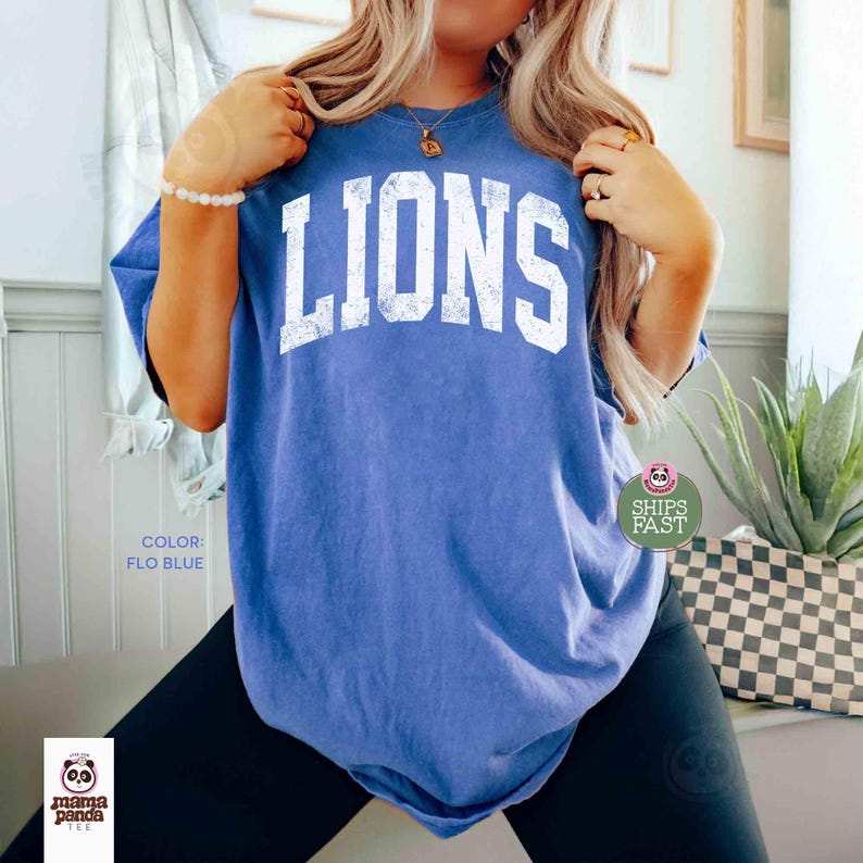 May include: Flo blue t-shirt with the word "LIONS" in white block letters. The shirt is a solid blue color and has a slightly faded, vintage look. The text "COLOR: FLO BLUE" is printed on the bottom left.