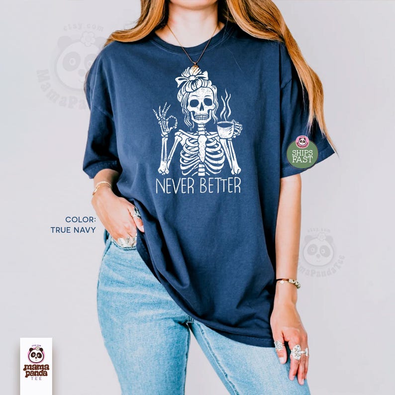May include: A true navy short-sleeve t-shirt featuring a white graphic of a skeleton with a messy bun hairstyle, holding a coffee mug and making an okay hand gesture. The text NEVER BETTER is printed in white below the skeleton illustration.