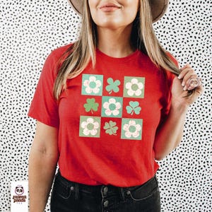 Op de afbeelding: Rood T-shirt met een groen en wit patroon van klavers en bloemen. Het patroon is in een raster van negen vierkanten.