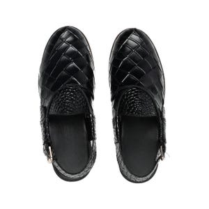 May include: A pair of black slip-on shoes featuring a woven leather-like upper with a glossy finish. The front section displays a grid-like pattern, while the tongue area has a textured, reptilian-inspired embossed design and a side buckle strap.