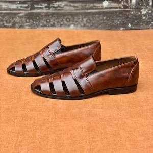 K&ouml;nnte beinhalten: Ein Paar braune Leder-Loafer im Huarache-Stil mit einem geflochtenen Riemendesign &uuml;ber dem Vorderblatt, einer geschlossenen Fersenkappe und einer flachen schwarzen Sohle. Das Leder hat ein poliertes, patiniertes Finish mit sichtbaren Farbnuancen.