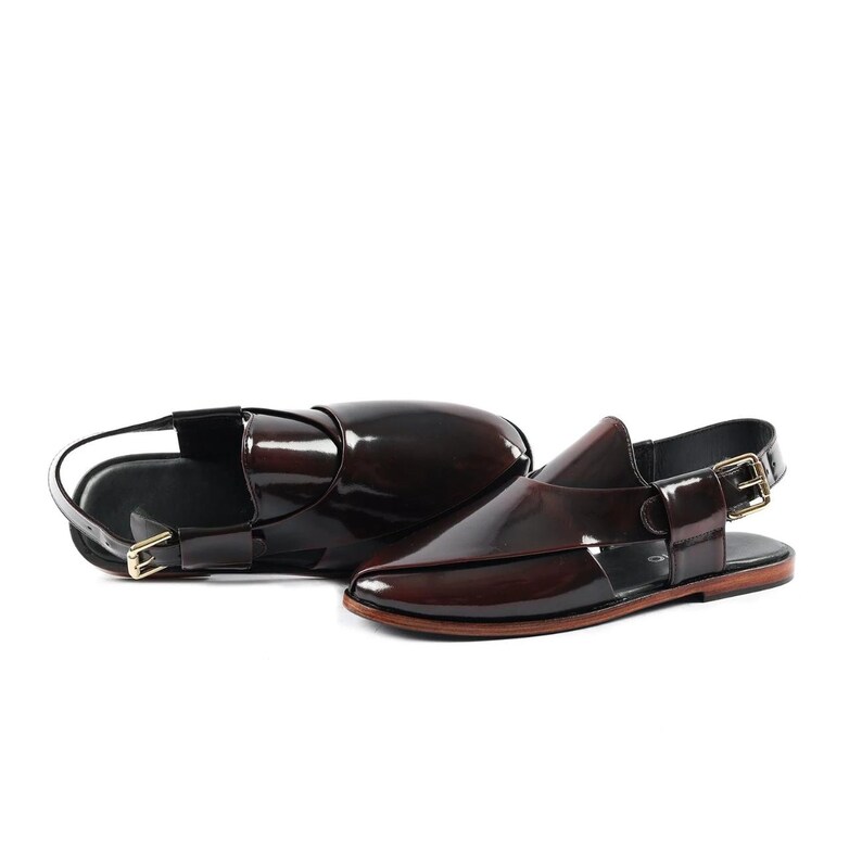 K&ouml;nnte beinhalten: Ein Paar dunkelburgunderfarbene, gl&auml;nzende Slingback-Sandalen aus Lackleder mit geschlossenem Zehenbereich, &uuml;berlappenden Riemen, einer goldfarbenen Metallschnalle an der Seite und einer flachen, d&uuml;nnen braunen Sohle. Das Schuhwerk ist poliert.