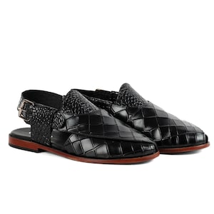 May include: A pair of black sandals featuring a woven-look textured upper with a crocodile-embossed strap and a metallic buckle closure. The footwear has a flat, dark brown sole and an open-heel design, showcasing a structured and polished appearance.
