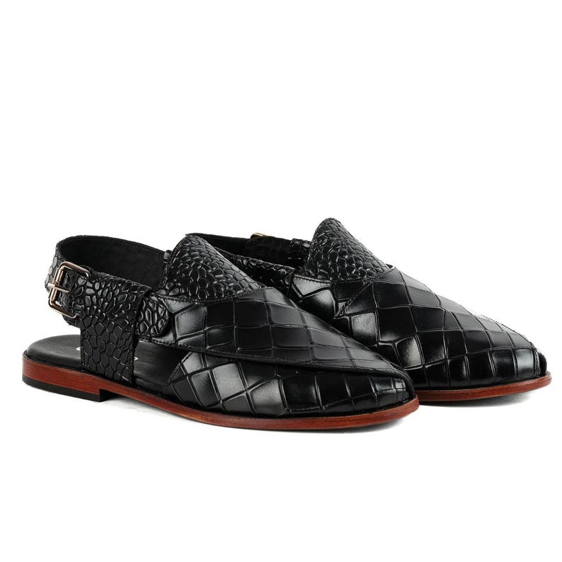 May include: A pair of black sandals featuring a woven-look textured upper with a crocodile-embossed strap and a metallic buckle closure. The footwear has a flat, dark brown sole and an open-heel design, showcasing a structured and polished appearance.