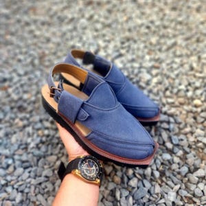 May include: A pair of blue leather sandals with a strap and buckle. The sandals have a brown sole and are made of a soft, comfortable material.