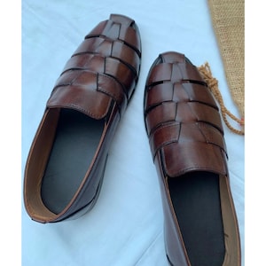 K&ouml;nnte beinhalten: Ein Paar dunkelbraune Leder-Loafer im Huarache-Stil mit geflochtenem Obermaterial aus breiten Riemen, einer geschlossenen Ferse und einem glatten, einfarbigen Innenfutter. Die Schuhe haben eine abgerundete Zehenpartie und eine polierte Oberfl&auml;che.