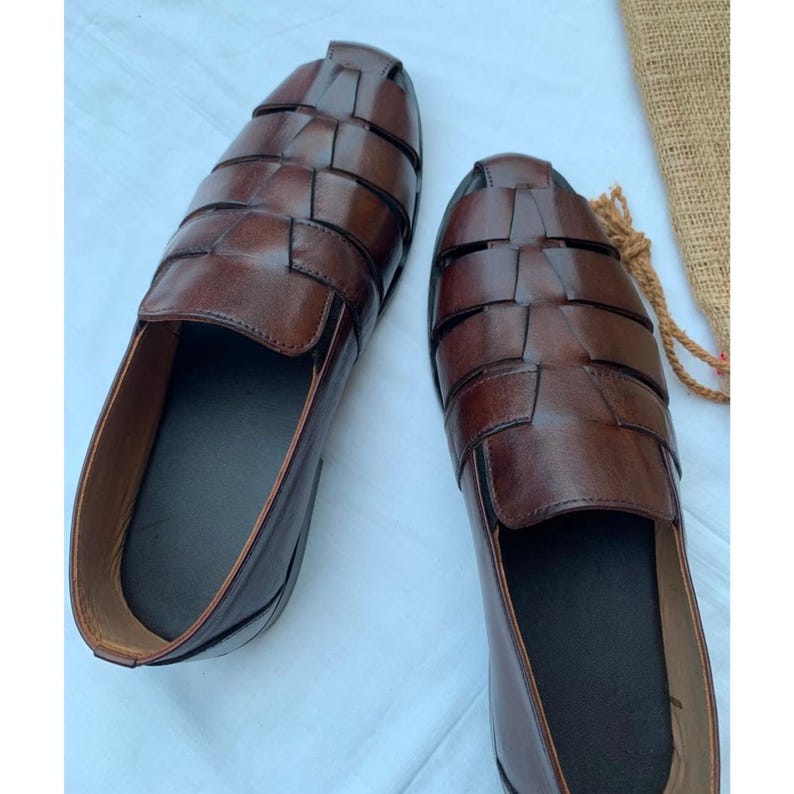 K&ouml;nnte beinhalten: Ein Paar dunkelbraune Leder-Loafer im Huarache-Stil mit geflochtenem Obermaterial aus breiten Riemen, einer geschlossenen Ferse und einem glatten, einfarbigen Innenfutter. Die Schuhe haben eine abgerundete Zehenpartie und eine polierte Oberfl&auml;che.