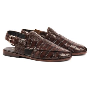May include: A pair of dark brown slingback sandals featuring a textured crocodile-embossed finish. The sandals have a closed-toe design with woven leather detailing, a side buckle closure, and a flat sole, providing a structured and polished appearance.