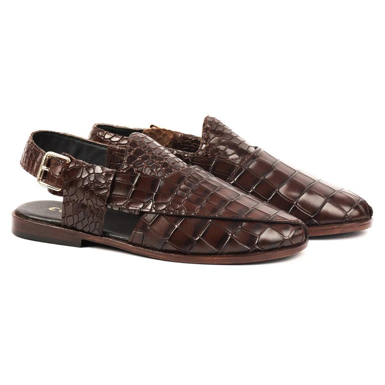 May include: A pair of dark brown slingback sandals featuring a textured crocodile-embossed finish. The sandals have a closed-toe design with woven leather detailing, a side buckle closure, and a flat sole, providing a structured and polished appearance.