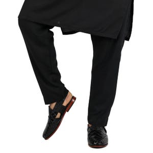 May include: Black trousers paired with black leather sandals featuring a textured crocodile-skin pattern, a closed-toe design with side cutouts, and a thin brown sole. The sandals have a slingback strap and a polished finish on the leather.
