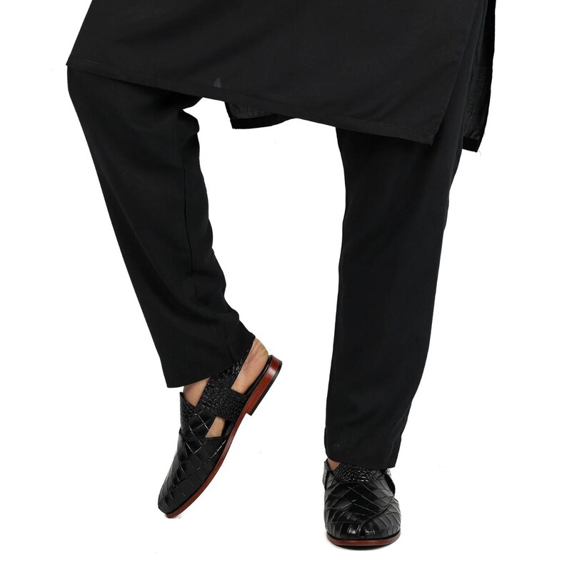 May include: Black trousers paired with black leather sandals featuring a textured crocodile-skin pattern, a closed-toe design with side cutouts, and a thin brown sole. The sandals have a slingback strap and a polished finish on the leather.