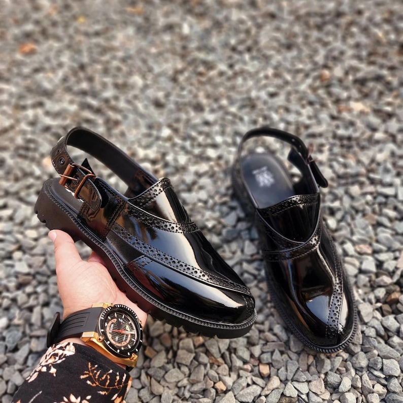 May include: A pair of black leather slip-on shoes with a buckle strap and a brogue design. The shoes have a glossy finish and a thick sole.