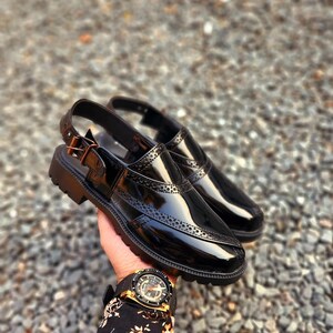 May include: A pair of black leather slip-on shoes with a buckle strap and a perforated design. The shoes have a glossy finish and a thick rubber sole.