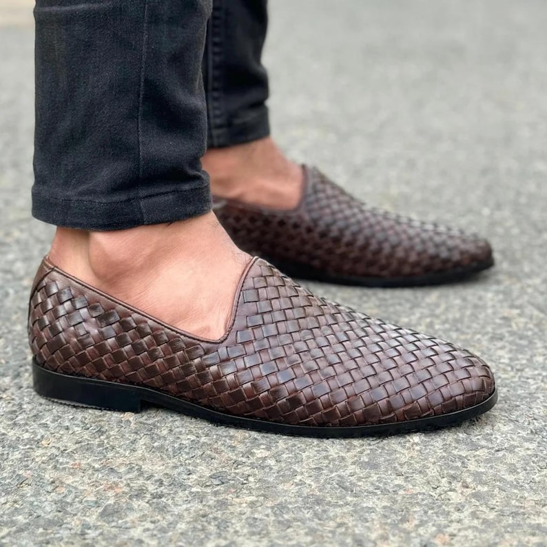 Pu&ograve; includere: Un paio di mocassini in pelle intrecciata marrone scuro con design slip-on, profilo basso e suola nera solida. La parte superiore della scarpa &egrave; realizzata con un motivo a intreccio stretto e complesso che copre l'intera superficie esterna.