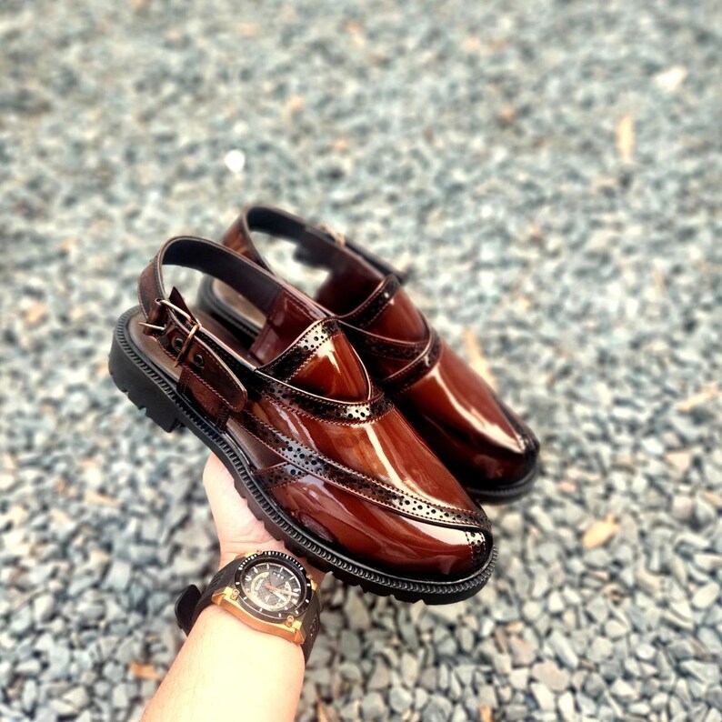 May include: A pair of brown leather sandals with a buckle strap and a perforated design. The sandals have a glossy finish and a black rubber sole.