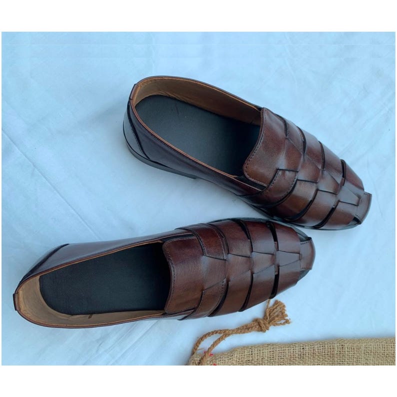 K&ouml;nnte beinhalten: Ein Paar dunkelbraune Leder-Loafer im Huarache-Stil mit einem geflochtenen Obermaterial aus breiten Riemen, einer geschlossenen Ferse und einem glatten Innenfutter. Die Schuhe haben ein Slipper-Design mit abgerundeter Zehenpartie und flacher Sohle.