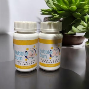 Può includere: Due flaconi di plastica bianca con etichette gialle. Le etichette recitano "Bubble Bum BUTT & HIPS ENHANCER" con un'illustrazione a cartoni animati. Ogni flacone contiene 60 capsule. I flaconi sono su una superficie riflettente.