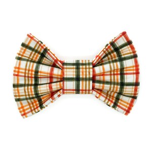 May include: A plaid bow tie in a fall color palette. The bow tie features a white background with a grid pattern of orange, green, and red lines. The bow tie is a classic accessory.