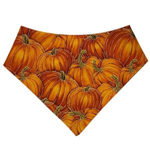 Könnte beinhalten: Ein Bandana mit einem sich wiederholenden Muster aus orangefarbenen Kürbissen mit grünen Stielen. Die Kürbisse sind in verschiedenen Größen und Ausrichtungen angeordnet und bilden ein herbstliches Design. Das Bandana hat eine dreieckige Form.