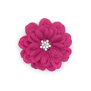 May include: A magenta fabric flower with layered petals and a sparkling rhinestone center. The flower is round and sits on a white background. This decorative flower could be used for crafts or as an embellishment.