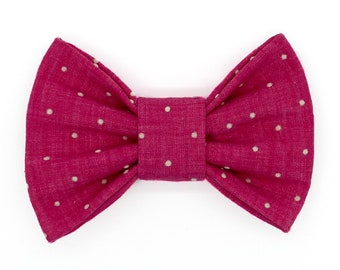 Op de afbeelding: Een magenta vlinderdas met kleine witte stippen. De vlinderdas is gemaakt van textiel met textuur en is in het midden geknoopt. De vlinderdas is een modeaccessoire.