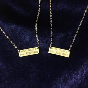 May include: Two gold necklaces with rectangular pendants that read "Nevertheless she persisted".
