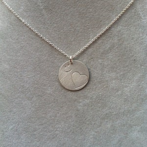 以下が含まれることがあります： ハートと笑顔が刻まれた丸いペンダントが付いたシルバーネックレスです。