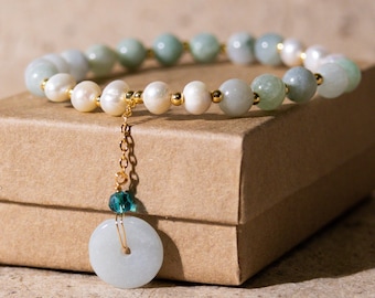 May include: A beaded bracelet featuring a mix of pale green jade and white pearls, accented with gold-colored beads. A gold chain suspends a jade pendant with a central hole. The bracelet is displayed on a brown box.