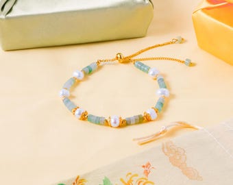 May include: A gold-tone adjustable bracelet featuring alternating white freshwater pearls and cylindrical green jade beads, accented with small gold-tone metal spacers and a sliding bead closure mechanism with dangling end beads.
