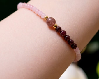 May include: A pink and red beaded bracelet with gold accents. The bracelet is made with small round beads and features a larger, round, brown bead in the center.