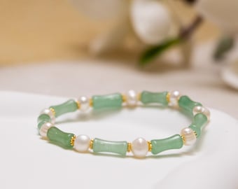 May include: A delicate bracelet featuring light green jade-like beads interspersed with white pearls. The bracelet has gold-colored accents and is set against a soft, blurred background. This elegant piece of jewelry is suitable for everyday wear or special occasions.