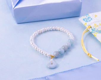 May include: A bracelet featuring a strand of small white freshwater pearls and four larger, smooth, light blue gemstone beads. A small gold-toned bead connects the strand to a circular, light blue gemstone pendant charm.