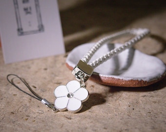 May include: White flower charm with a rhinestone center attached to a white braided cord with a silver clasp. The charm is attached to a black cord.