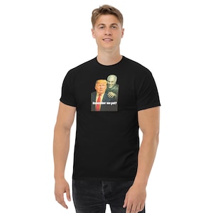 Könnte beinhalten: Schwarzes T-Shirt mit einer Grafik von zwei Figuren, von denen eine einem ehemaligen US-Präsidenten und die andere einer geisterhaften Figur ähnelt. Der Text "Remember me pal?" steht darunter. Das T-Shirt wird von einer Person getragen.