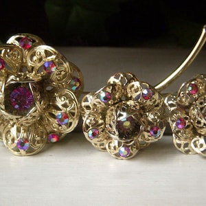 K&ouml;nnte beinhalten: Ein Set aus drei goldfarbenen Broschen in Blumenform mit schillernden rosa Strasssteinen.