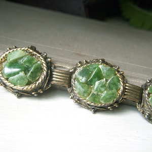 May include: A vintage bracelet with green jade stone accents. The bracelet is made of gold-toned metal and features a series of oval-shaped stones.