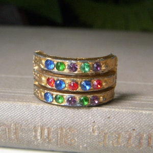 May include: A gold-toned ring with three bands of colorful rhinestones. The rhinestones are red, blue, green, and purple.