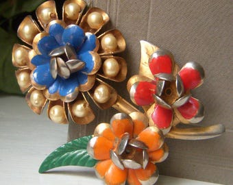 May include: Three vintage floral brooches. One brooch features a blue flower with faux pearls and gold-tone petals. Another has red and silver petals. The third brooch has orange petals. A green leaf is also present.