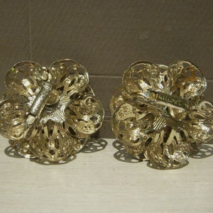 K&ouml;nnte beinhalten: Ein Paar goldfarbene Ohrclips mit einem filigranen Design. Die Ohrringe sind blumenf&ouml;rmig mit filigranen Details.