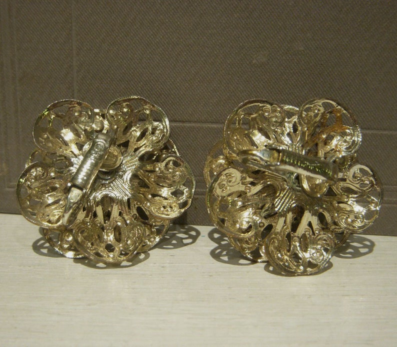 K&ouml;nnte beinhalten: Ein Paar goldfarbene Ohrclips mit einem filigranen Design. Die Ohrringe sind blumenf&ouml;rmig mit filigranen Details.