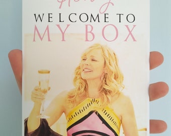 May include: A greeting card with the words "Honey Welcome to My Box" in pink and black text. The card features an image of a woman holding a champagne glass, wearing a colorful top.