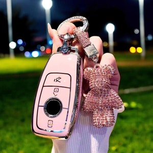 May include: Pink car key chain with a sparkly pink bear charm. The key chain is made of metal and has a silver ring. The bear charm is covered in rhinestones.