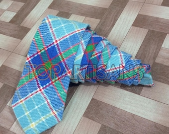 May include: A blue, green, red, and white plaid tie. The tie is folded and laid on a brown and white patterned surface.