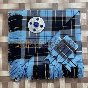 May include: A blue and black plaid kilt with a matching bow tie and a silver brooch with blue accents. The kilt has a fringed edge and a yellow stripe in the plaid pattern. The text "TOP ARTISANS" is visible.